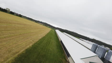 FPV-Drohnenflug-über-Ein-Ackerfeld-Mit-Stall-Für-Tiere-Bei-Grauem-Himmel-Auf-Dem-Land-Einer-Amerikanischen-Stadt