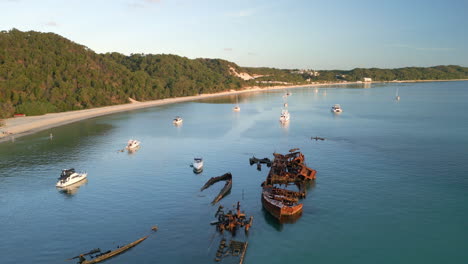 Los-Barcos-Flotan-Todavía-Alrededor-Del-Naufragio-En-El-Paisaje-De-Colinas-Boscosas-De-La-Isla-Tangalooma-Moreton,-Drones-Aéreos-Volando-Lento