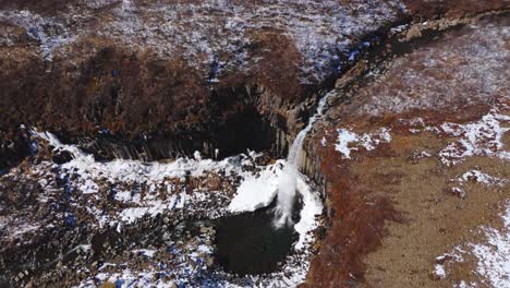 Cascading-water-aerial-top-down-view-Svartifoss-Waterfall-Iceland-Black-Hidden-Iced-landscape,-around-earthy-volcanic-soil