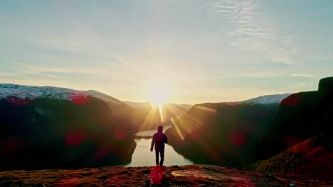 Man-Walks-towards-the-sunset-skyline-mountain-range-lake-drone-shot-from-behind