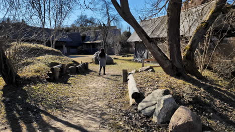Woman-Walking-Towards-The-Old-Wooden-Buildings-At-Open-air-Museum