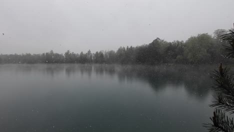 Große-Schneeflocken-Fallen-Auf-Einen-Mystischen-See-Mit-Kiefern-Im-Vordergrund-Und-Wald-Im-Hintergrund