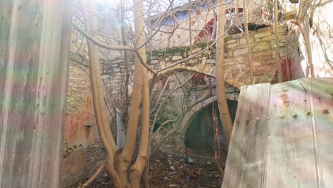 Peering-through-a-weathered-doorway-into-an-overgrown-courtyard,-with-a-glimpse-of-an-old-stone-building-and-bare-tree-branches