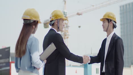 Business-Building-Partners-Shaking-Hands-In-Helmets-With-Documents-Checking-Plans-At-Construction-Site