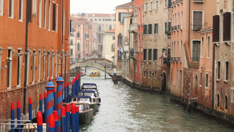 Boat-passing-under-bridge,-boats-anchored-next-to-houses,-Venice-canal,-Italy