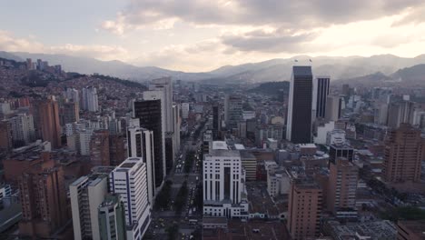 Dusk-descending-on-Medellin's-modern-skyline-and-mountain-surrounds,-Colombia---aerial