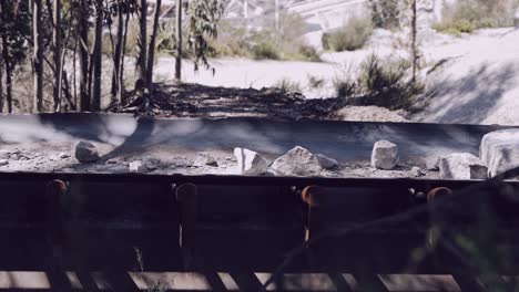 Close-up-of-rocks-on-a-mining-conveyor-belt-against-a-wooded-backdrop