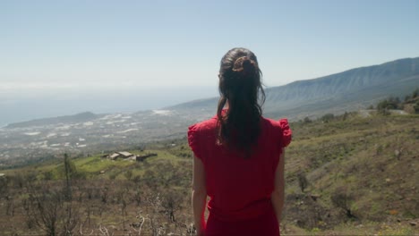 Young-woman-tourist-in-red-dress-looking-at-dry-landscape-of-southern-Tenerife,-Canary-Islands-in-spring
