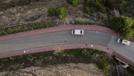 Get-a-bird's-eye-view-of-the-road-at-Malaga-with-drone-footage-capturing-a-parked-white-four-wheeler-and-another-vehicle-passing-by