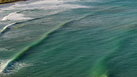 Einsamer-Surfer-Sitzt-Wartend-In-Der-Mitte-Der-Bucht,-Während-Wellen-überrollen-Und-Brechen