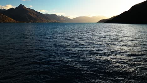 Aerial-dolly-above-Lake-Wakatipu-water-ripples-on-surface-at-sunset-with-mountain-flare