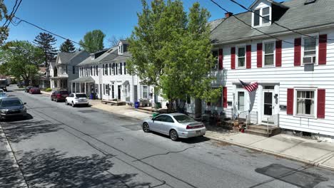 Pickup-Truck-driving-on-road-in-small-american-town-with-flag-of-USA-on-House-facade