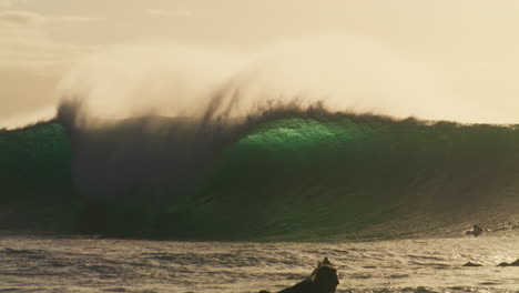 Surfers-quickly-paddle-to-get-out-of-impact-zone-of-huge-glistening-wave