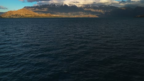 Lake-Wakatipu-with-snowcapped-mountains-and-thick-long-grey-clouds-in-distance