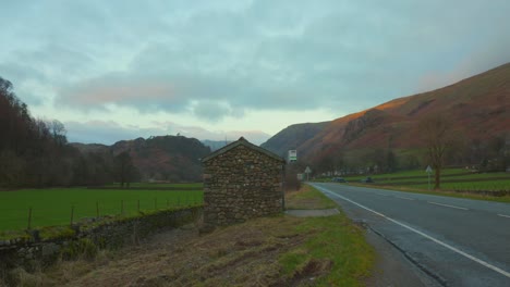Stone-shed-by-countryside-road-with-cars-in-England-on-cloudy-day