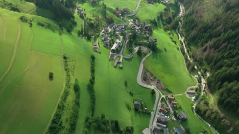 A-tilt-down-aerial-view-of-the-winding-roads-cutting-through-the-steep-grass-covered-hills-of-the-small-village-of-La-Val,-South-Tyrol,-Italy
