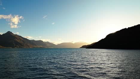 Atemberaubende-Sonne-Flare-Zieht-Sich-Hinter-Hügel-über-Lake-Wakatipu-Mit-Großen-Bergen