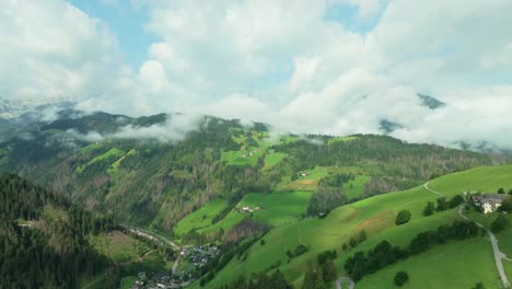 A-drone-is-flying-fast-towards-a-small-settlement-on-a-lush-green-hill-covered-in-clouds