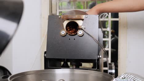 Industrial-coffee-roasting-machine,-hot-vaping-barista-equipment-pouring-grains-into-big-pan,-making-process