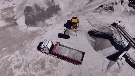 Aerial-shot-of-an-industrial-loader-filling-a-truck-with-gray-sand-at-a-quarry