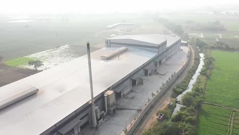 aerial-drone-view-drone-camera-moving-forward-showing-a-large-factory-and-behind-the-factory-a-small-river