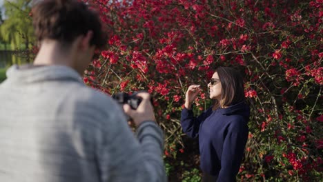 Photographer-with-digital-camera-do-photo-shoot-with-woman-near-blooming-shrub