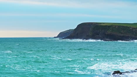 Seafoam-green-ocean-waters-churn-rocky-and-rough-across-surface-below-cliffs