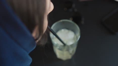 High-angle-view-of-female-drink-cold-lemonade-with-ice-cubes-with-straw