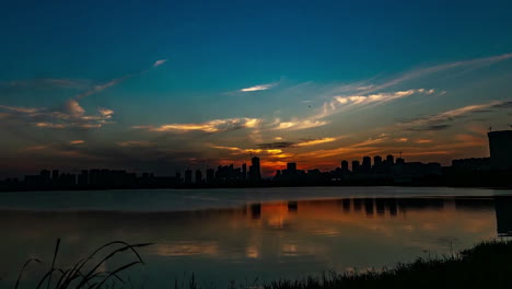 Siluetas-De-Lapso-De-Tiempo-Con-Colorida-Puesta-De-Sol-Sobre-Un-Pequeño-Lago-Cerca-De-La-Ciudad,-Video-De-Noche-De-Verano