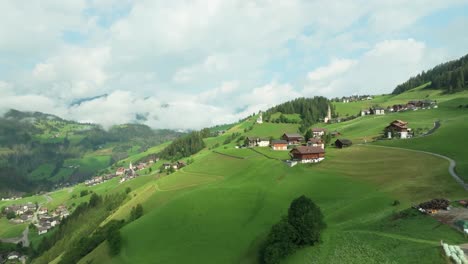 Flying-above-lush-greenery-towards-a-church-on-the-steep-slopes-of-the-village-of-La-Va,-South-Tyrol,-Italy