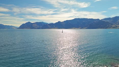 Panoramic-aerial-pullback-above-rocky-island-with-sailboat-and-mountain-peak-landscape