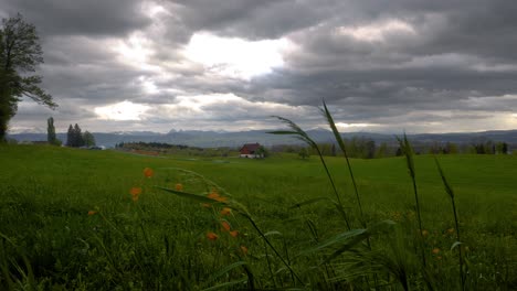 Grey-storm-clouds-gather-above-peaceful-farm-house-in-grassy-field,-Baretswil,-Switzerland