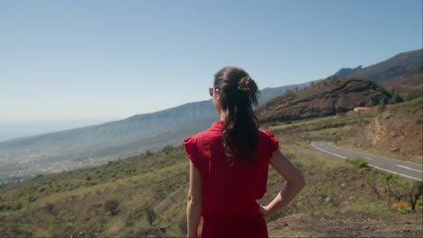 Young-woman-in-red-dress-looking-at-dry-landscape-of-southern-Tenerife,-Canary-Islands-in-spring