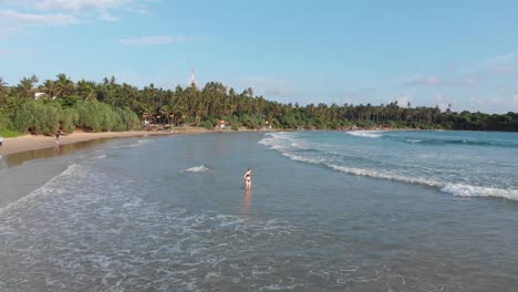 Drohne-Fliegt-über-Frau,-Die-Im-Seichten-Wasser-Des-Strandes-Von-Hiriketiya-In-Sri-Lanka-Steht