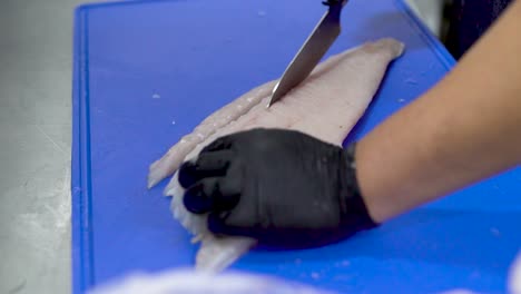 Kochhände-Mit-Schwarzen-Handschuhen-Schneiden-Fisch-Auf-Einem-Blauen-Schneidebrett