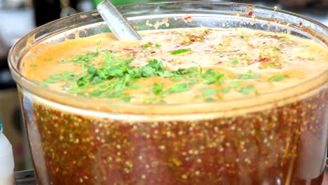 The-bowl-contains-a-Thai-style-chili-soup,-its-fiery-broth-adorned-with-tantalizing-toppings,-Emanating-intense-spiciness,-this-soup-promises-a-flavorful-and-aromatic-sensation