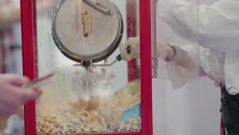 Fresh-popcorn-bursts-in-a-red-vintage-machine-as-an-attendant-scoops-it-up,-a-classic-snack-in-the-making