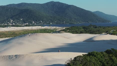 A-couple-strolling-on-the-sand-dunes-of-Joaquina-Beach-in-Florianópolis,-Brazil