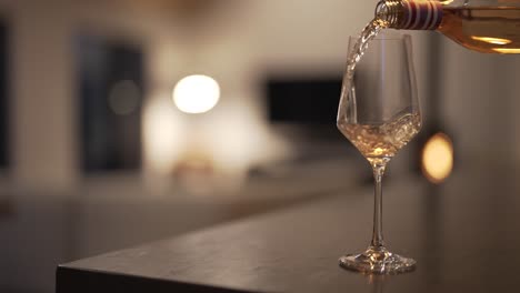 Zeitlupe-Einer-Flasche-Weißwein,-Die-In-Ein-Glas-Gegossen-Wird,-Mit-Verschwommenem,-Schickem-Wohnzimmer-Im-Modernen-Haus-Im-Hintergrund