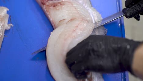 Chef-hands-with-black-gloves-skinning-fish-fillet-with-a-Sharp-knife-on-a-blue-cutting-board