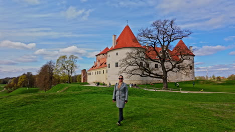 Lonely-Woman-Walking-on-Grass-in-Front-of-Historic-Bauska-Castle-Museum,-Latvia