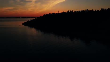 Drone-rising-over-forest,-revealing-idyllic-archipelago,-Finland,-summer-sunset