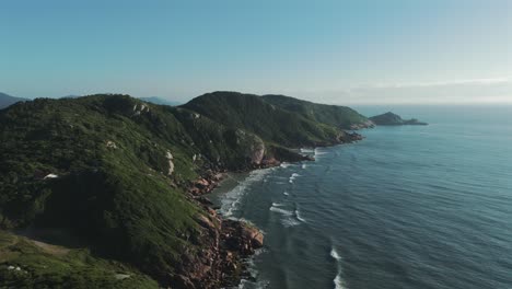 A-breathtaking-aerial-view-captures-the-rugged-beauty-of-Joaquina's-rocky-coastline,-where-the-mighty-Atlantic-Ocean-meets-the-land,-creating-a-mesmerizing-vista-of-natural-splendor