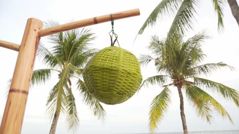 Woven-straw-decoration-hang-on-bamboo-pole-with-palm-trees-in-background