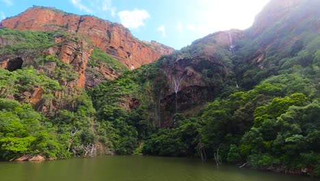 Mountain-with-green-forest-and-waterfall-approach-on-water,-South-Africa