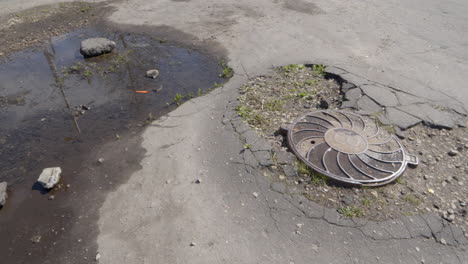 Trampilla-De-Drenaje-Rota-Con-Grietas-En-Caminos-De-Asfalto-Pasarela-Peatonal,-Toma-Panorámica