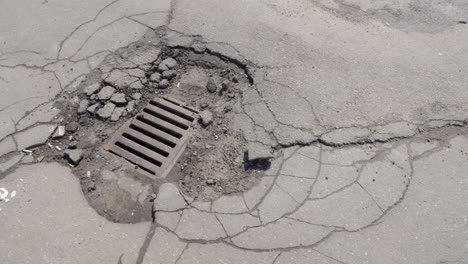 Cracked-ruined-drain-hatch-asphalt-pit-roads-pedestrian-walkway,-panning-shot