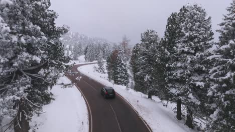 Following-drone-shot-of-black-car-on-mountain-road-during-peaceful-winter-day-in-Italy