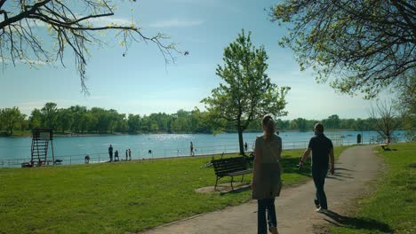 Ruhiger-Tag-Am-Jarun-See,-Mit-Menschen,-Die-Vor-Einem-Klaren-Blauen-Himmel-In-Zagreb,-Kroatien,-Spazieren-Gehen-Und-Die-Uferpromenade-Genießen