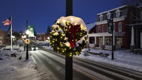 Christmas-wreath-covered-in-snow-in-American-town-with-flag-waving-in-background